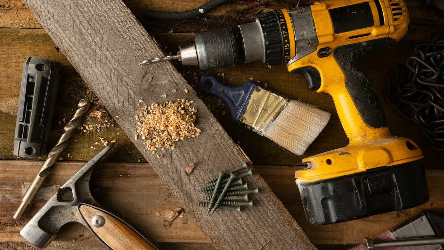 Hand tools and a cordless drill laid out on a workbench
